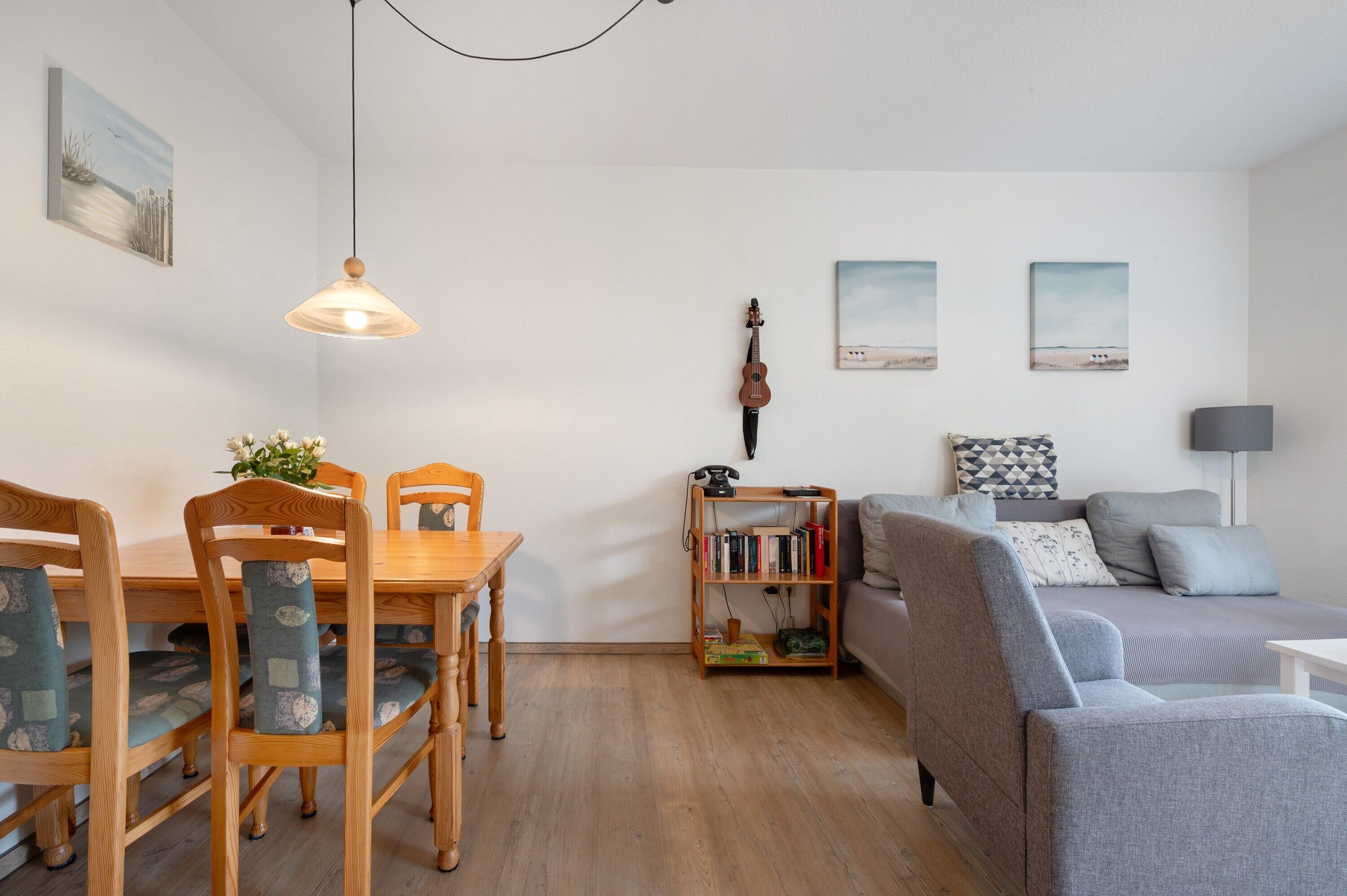Een woonkamer met een houten eettafel, stoelen, een grijze bank, een boekenkast en een hangende viool.