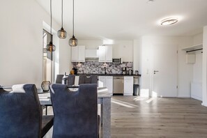 Una cocina moderna con armarios blancos, salpicadero de piedra e iluminación colgante.