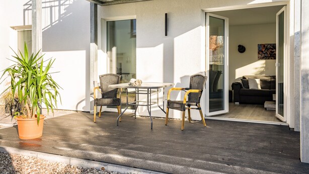 Een buitenpatio met een tafel en stoelen, een bloempot en een blik op een woonkamer binnen.