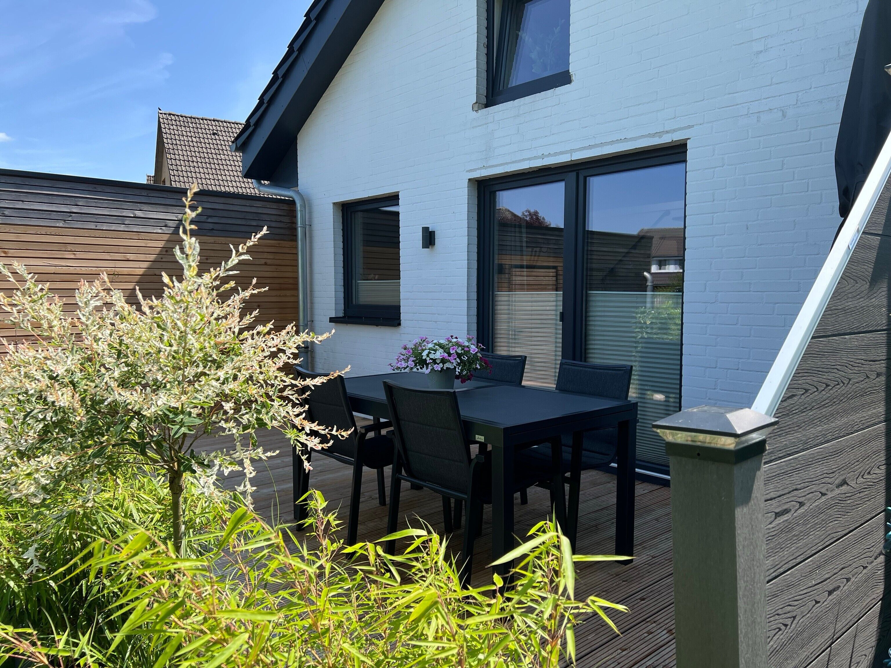 A patio with a table and chairs, a white building with a window, and a wooden fence.