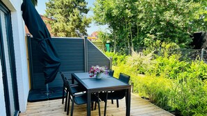 Une terrasse extérieure avec une table et des chaises, entourée de verdure et d’une clôture.