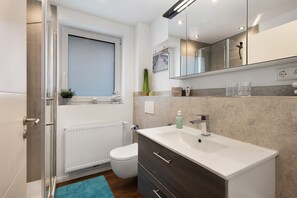 A modern bathroom with a white sink, dark wood cabinet, and a large mirror. - Holiday Home 'Küsten-Bude' with Private Terrace, Garden, and Wi-Fi (Elmenhorst)