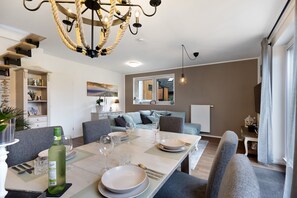 A dining area with a table set for four, a chandelier, and a view of the living room. - Holiday Home 'Küsten-Bude' with Private Terrace, Garden, and Wi-Fi (Elmenhorst)