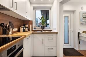 Una cocina moderna con armarios blancos, encimera de madera, horno empotrado, cafetera y ventana con vistas a edificios.