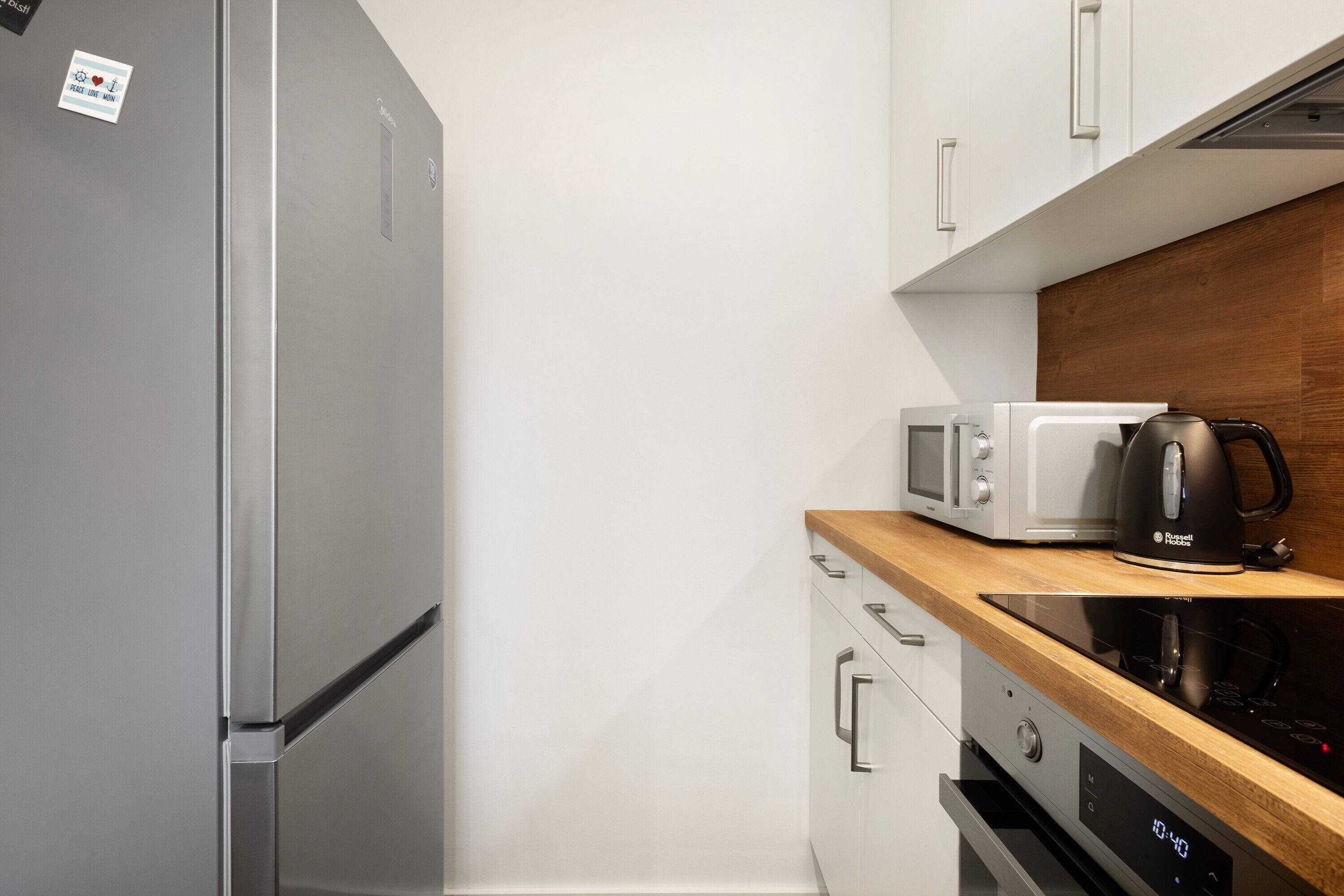 Eine moderne Küche mit einem Edelstahl-Kühlschrank, einer Mikrowelle, einer Kaffeemaschine und einem Induktionskochfeld.