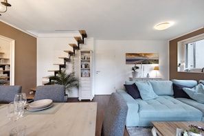 En moderne stue med sofa, spisebord og trappe med indbyggede hylder.