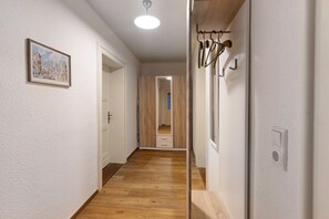 Un couloir avec un plancher en bois, une porte à gauche, un porte-manteau à droite et un tableau encadré au mur.