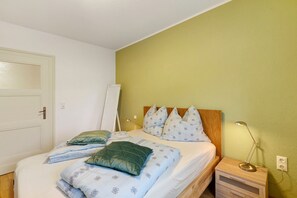 Une chambre à coucher avec un lit, des oreillers, une table de chevet, une lampe et une porte.