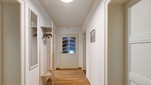 Un couloir avec un plancher en bois, des murs blancs, une porte avec une fenêtre et un porte-manteau.