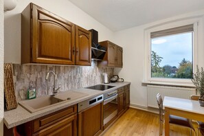Una cocina con armarios de madera, horno empotrado, un lavamanos y una ventana con vistas a árboles.