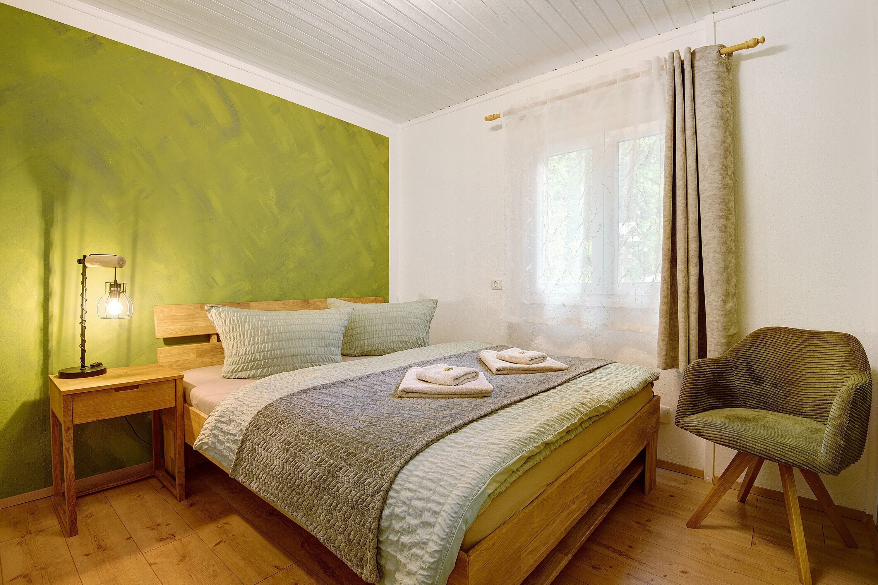 A bedroom with a bed, bedside table, chair, and a window with curtains.