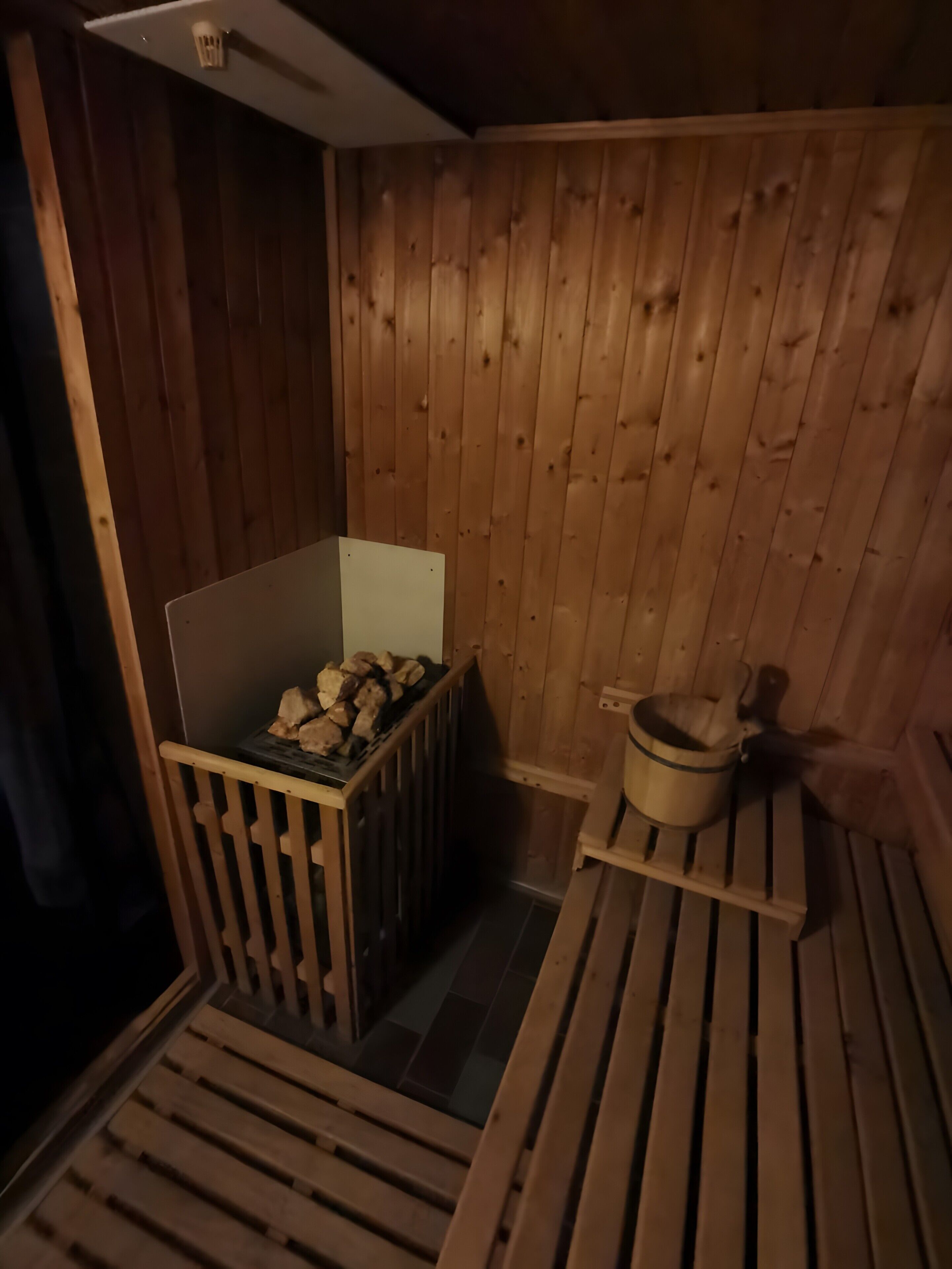 A sauna room with wooden walls, a bench, a bench with a bucket, and a box of firewood.