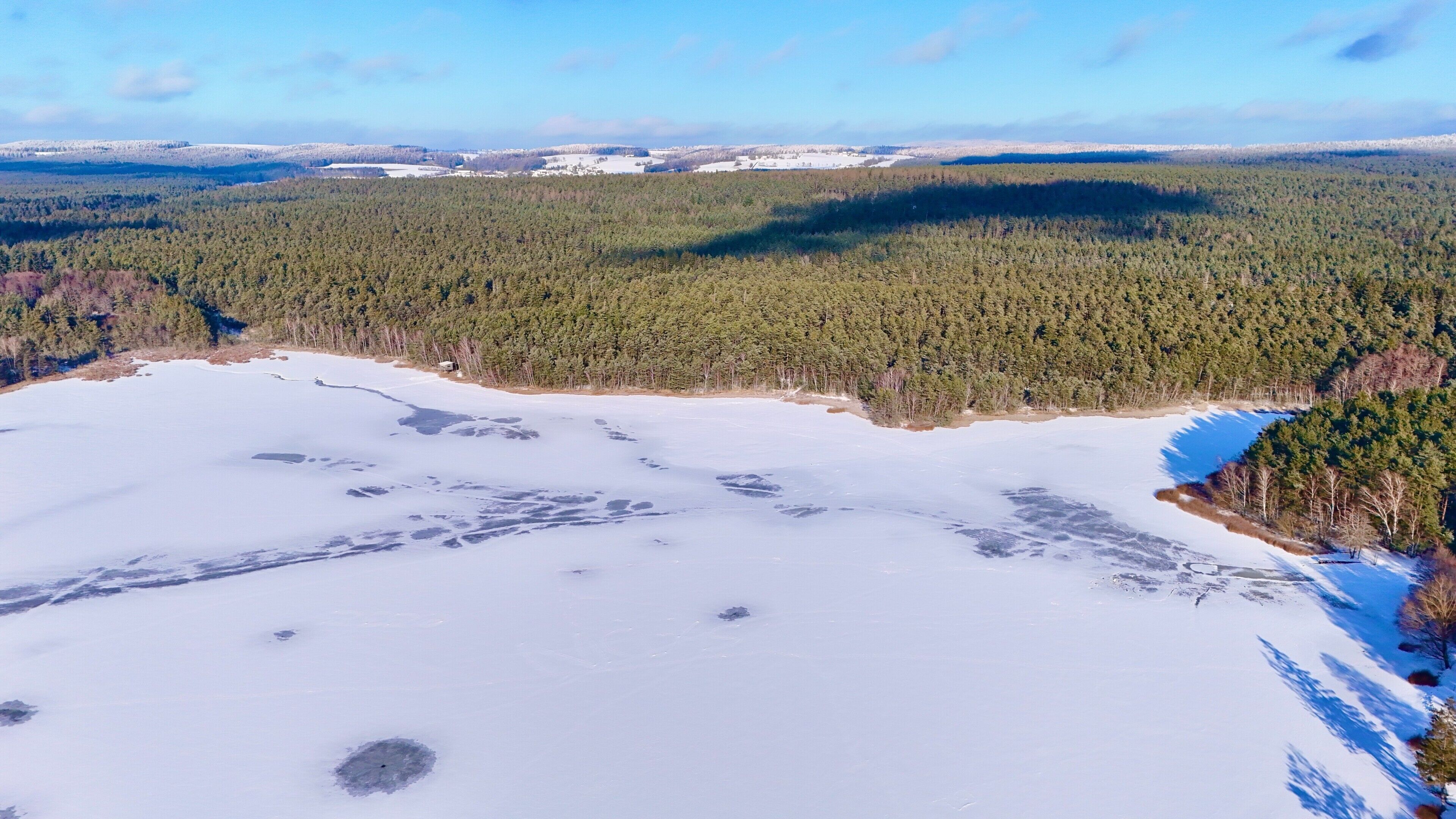 A snow-covered landscape with a dense forest and a frozen lake.