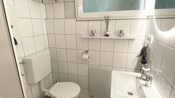 Une salle de bain équipée de toilettes, d’un lavabo, d’un miroir et d’une plante suspendue.