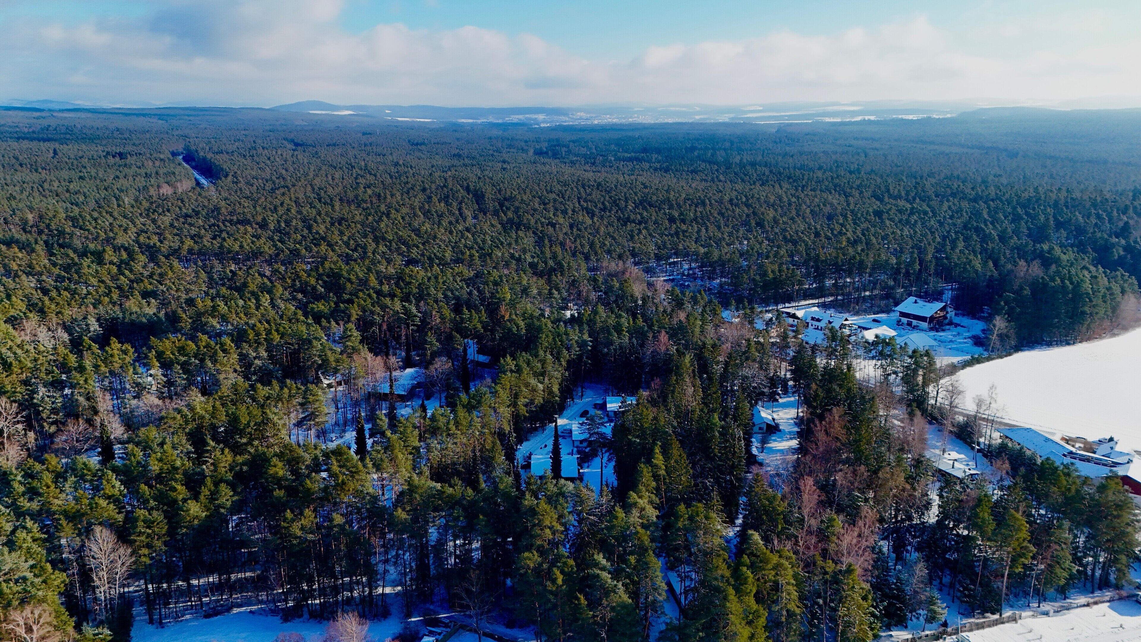 An aerial view of a forested area with a snow-covered landscape and buildings.