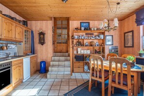 Une cuisine en bois équipée d’un fourneau, de placards et d’un coin repas avec des chaises et une table.