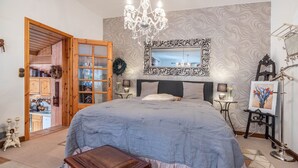 Une chambre à coucher avec un grand lit, un lustre, un miroir et une porte en bois donnant sur la cuisine.