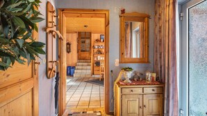 Un intérieur en bois avec une porte donnant sur un coin repas, un miroir au-dessus d’un meuble en bois et une plante sur la gauche.