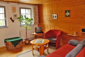 Een gezellige kamer met houten details, een rode bank, een televisie, een tafeltje en een plant in een pot.