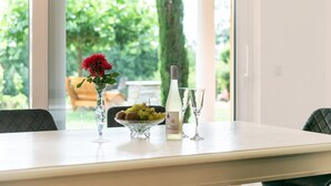 Una mesa de comedor con un jarrón de flores rojas, un frutero, una botella de vino y dos copas.