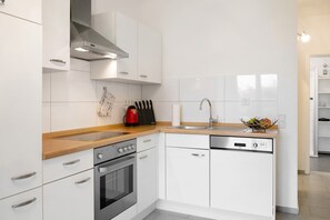 Una cocina moderna con armarios blancos, electrodomésticos de acero inoxidable, encimera de madera y lavavajillas integrado.