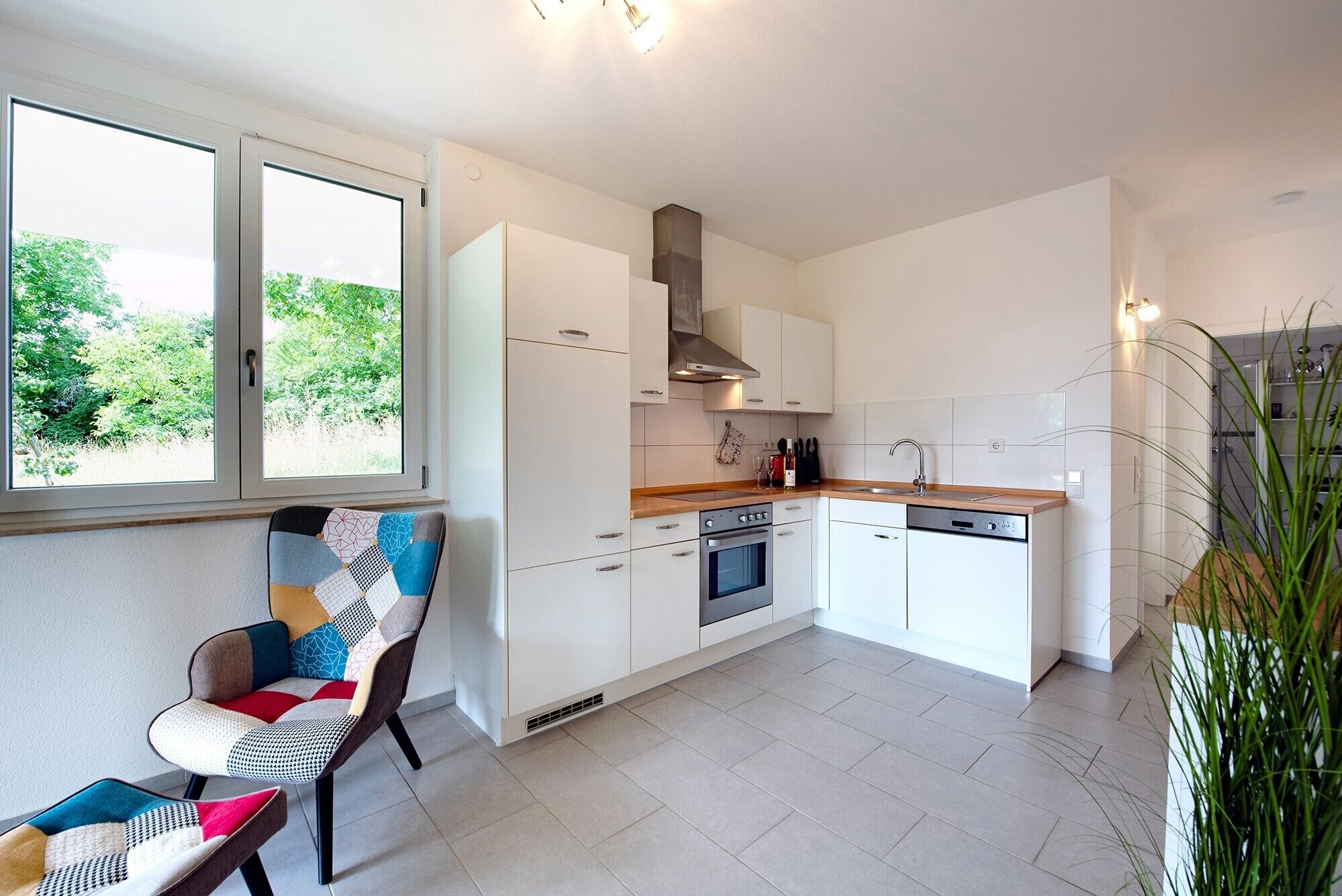 Een moderne keuken met witte kastjes, een ingebouwde oven en een raam met uitzicht op groen.