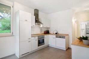 Una cocina moderna con gabinetes blancos, una campana extractora de acero inoxidable, horno empotrado y lavavajillas.