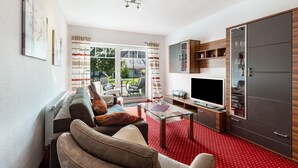 Un salon avec un canapé, un téléviseur et une table basse en verre. Il y a une porte coulissante qui donne sur l’extérieur.