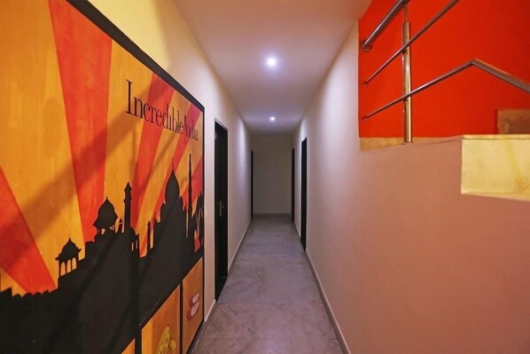 A hallway with a carpeted floor, a staircase with a red wall, and a poster with a cityscape and text. - Hotel Ganpati Palace Agra (Agra)