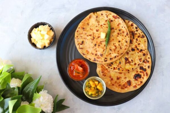 A plate with two flatbreads, a small bowl of butter, and two small bowls of chutney and pickle. - Hotel Ganpati Palace Agra (Agra)