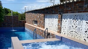 Een zwembad met een whirlpool, omringd door een bakstenen muur met decoratieve witte panelen.