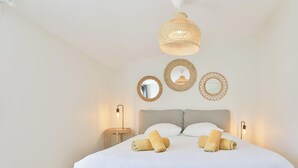 Une chambre à coucher comprenant un lit, deux lampes de chevet, un luminaire suspendu et trois miroirs fixés au mur.