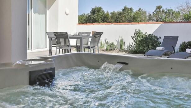 Un bain à remous rempli d’eau, une table avec des chaises et un espace détente avec des fauteuils.
