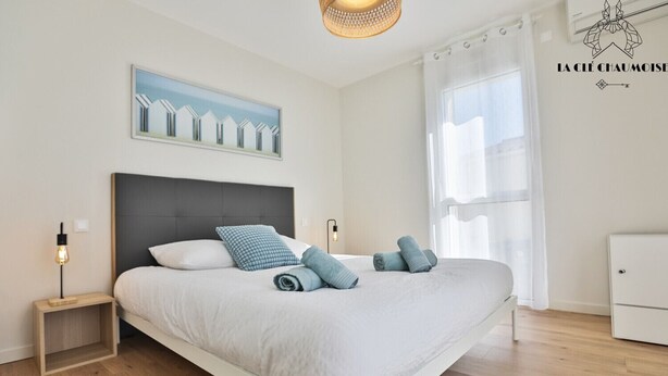 Un dormitorio moderno con una cama, dos mesitas de noche, una lámpara de pared, un cuadro y una ventana con cortinas.