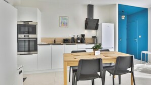 Una cocina moderna con armarios blancos, una mesa de comedor de madera, sillas negras y una puerta azul.