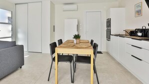 Una cocina moderna con armarios blancos, una mesa de comedor con cuatro sillas, un sofá gris y una pequeña planta en maceta sobre la mesa.