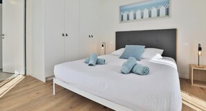 Une chambre moderne avec un grand lit, des murs blancs et un tableau accroché au-dessus.