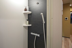 Ett modernt badrum med dusch, en vit hylla med toalettartiklar och en mörk, strukturerad vägg.