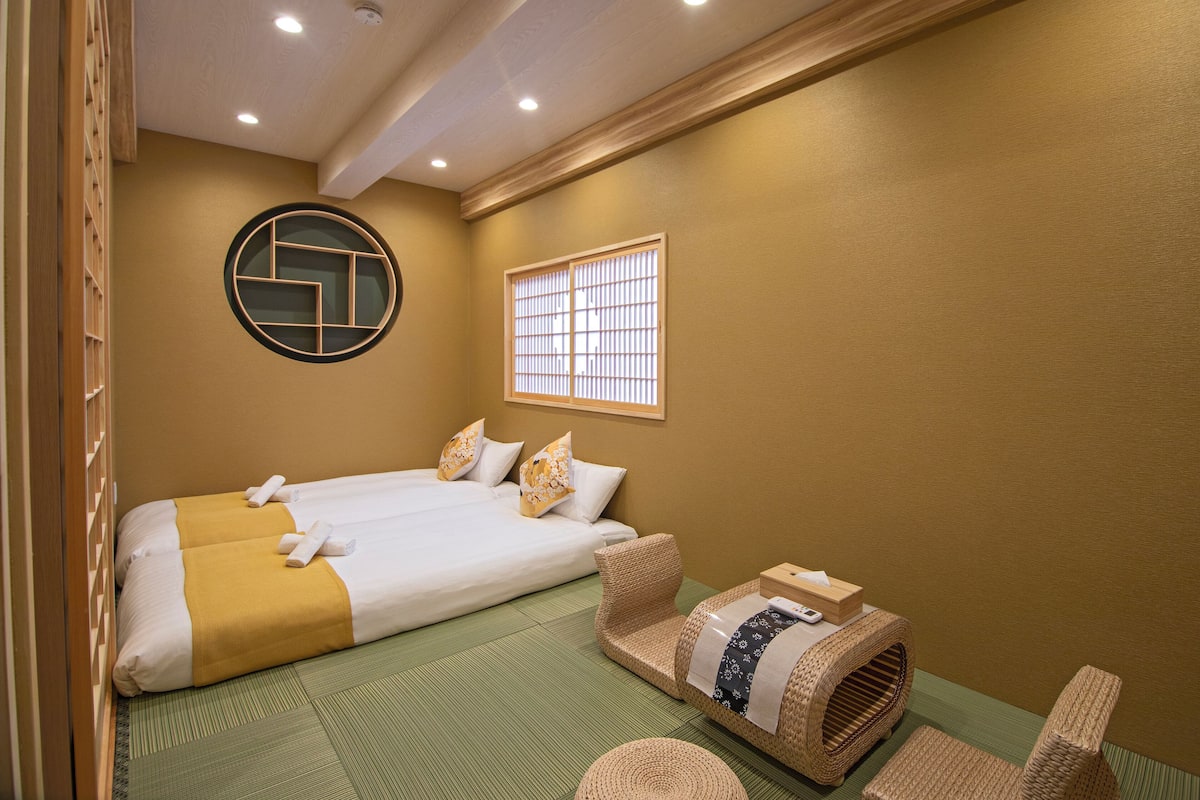 Quarto de hotel com duas camas, piso de esteira de tatame, janela no estilo tradicional japonês e uma cesta de palha.