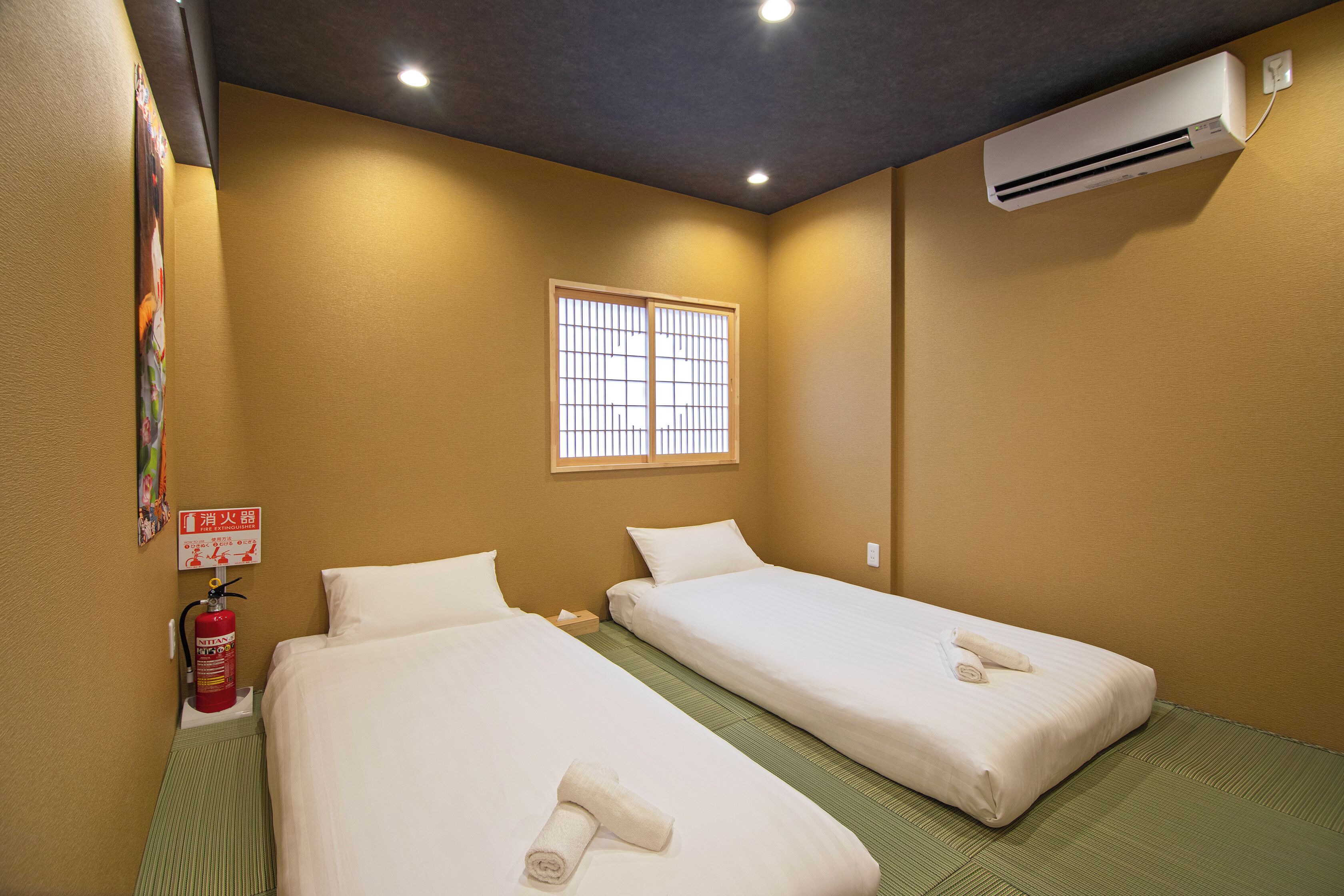 Habitación de hotel con dos camas, una ventana, aire acondicionado y extintor.