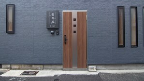 A building facade with a textured blue wall, a wooden door with a metal handle, and a sign above the door. - Travel time Setsugekka (Osaka)