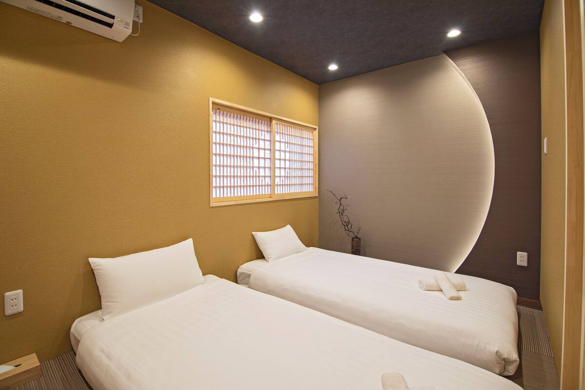 Quarto de hotel com duas camas, janela com persianas, ar condicionado e design de parede curva.