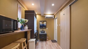 A modern kitchen with wooden stools, a built-in microwave, and a small refrigerator. - Travel time Setsugekka (Osaka)