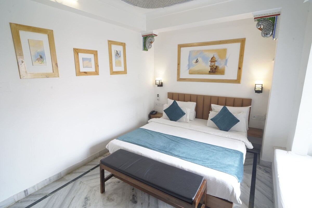 A bedroom with a bed, bedside tables, a bench, and framed pictures on the wall.
