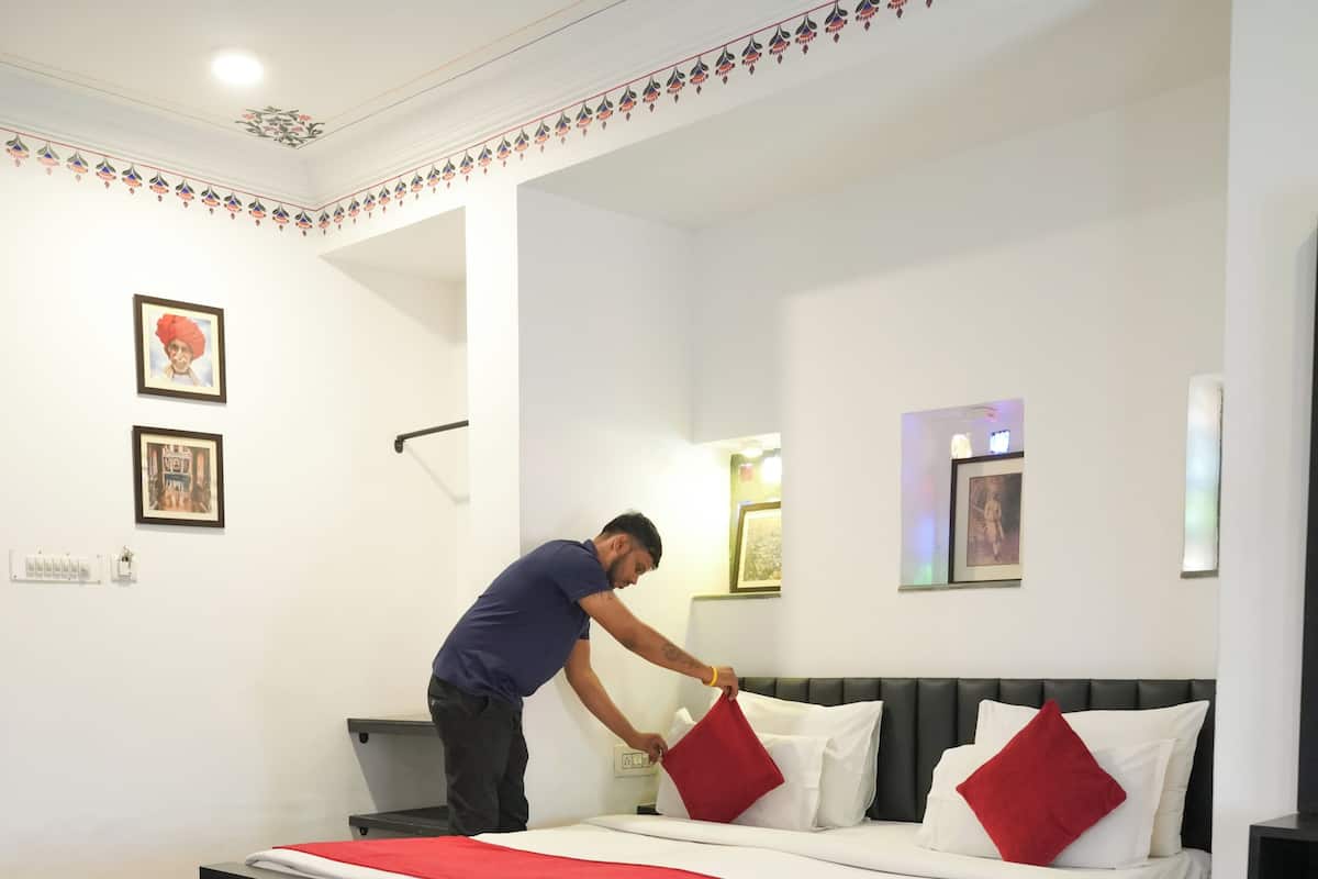 A hotel room with a bed, bedside tables, a small table with a book and remote controls, and a ceiling fan.