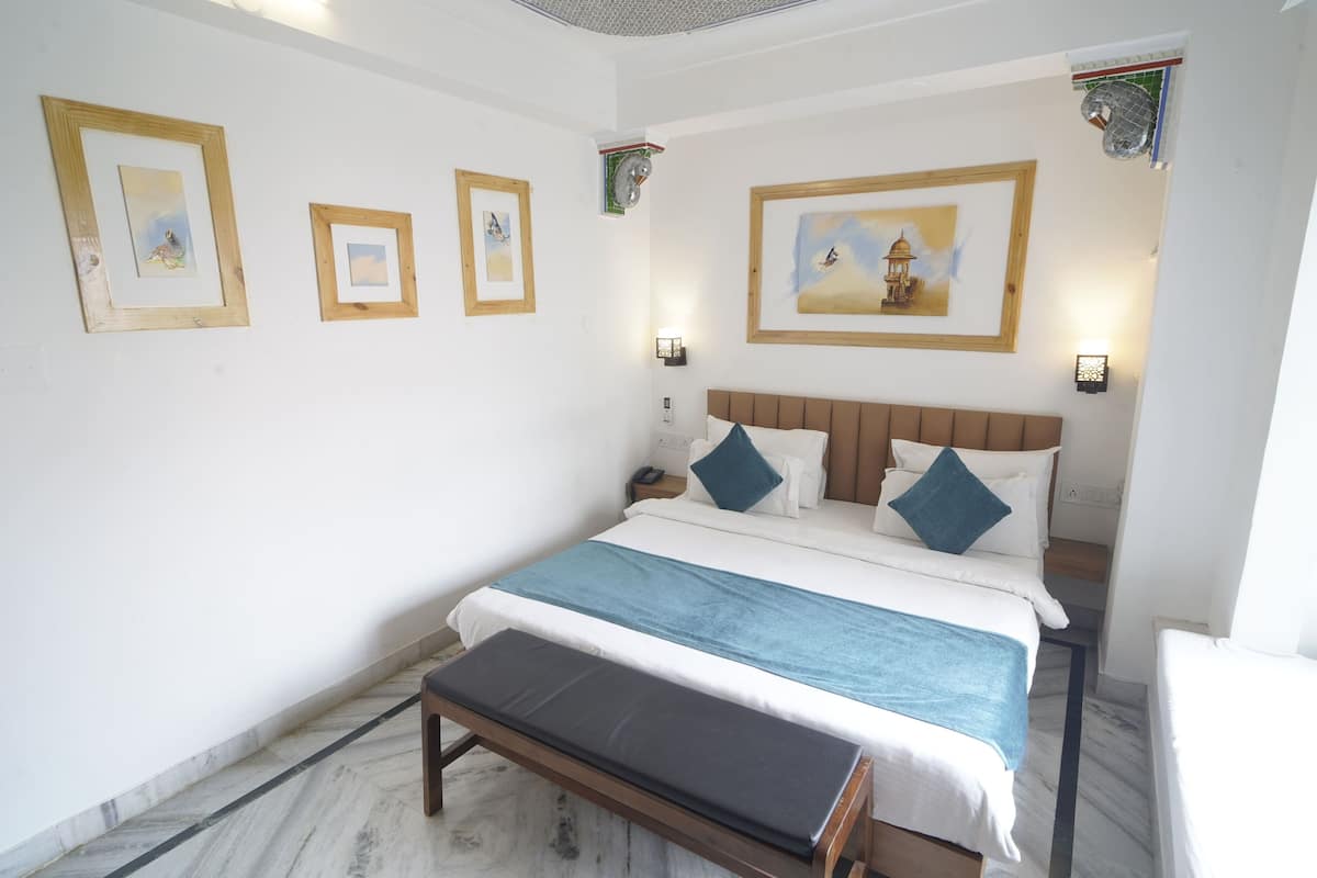 A bedroom with a bed, bedside tables, a bench, and framed pictures on the wall.