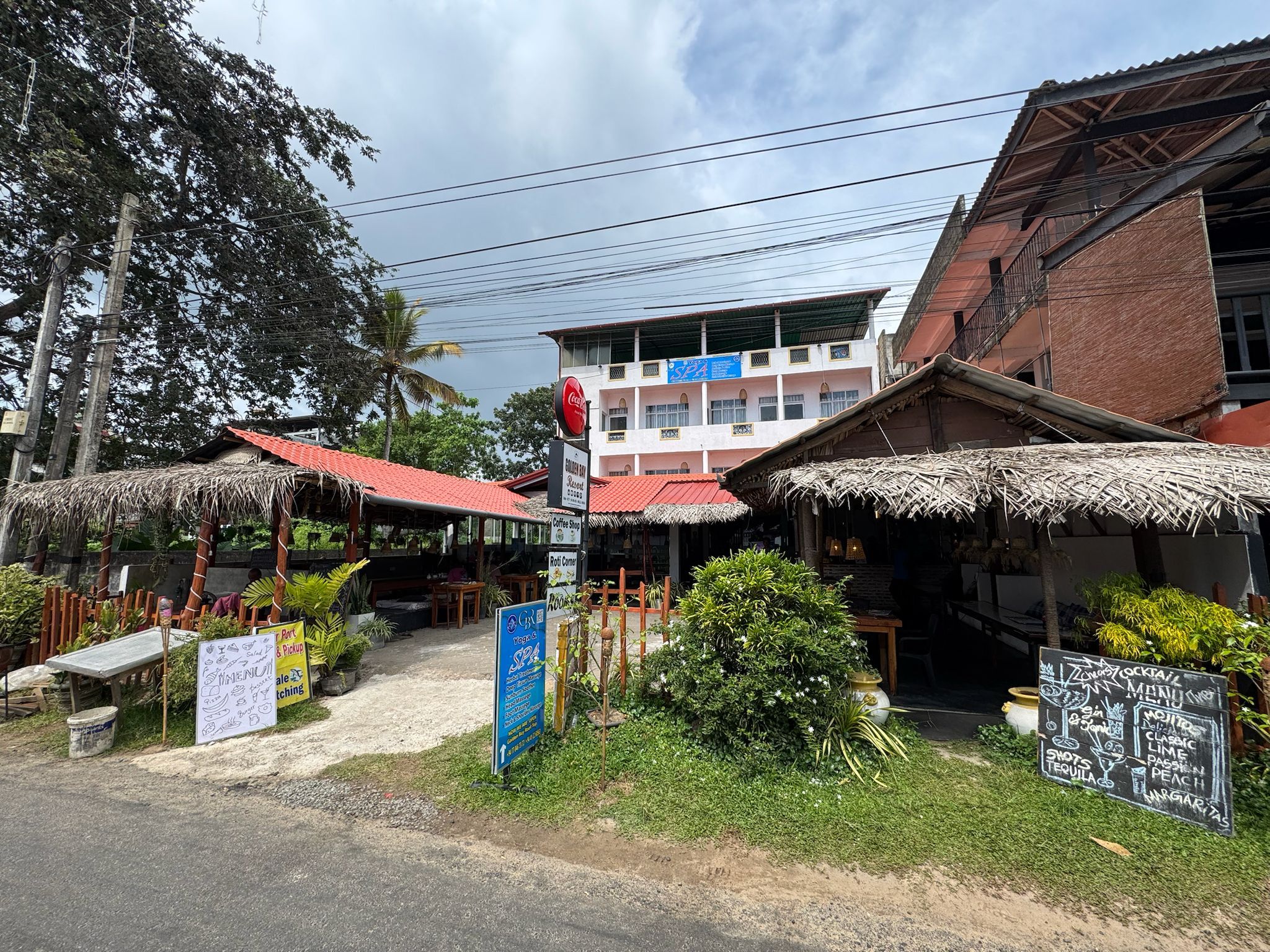 A restaurant with outdoor seating, a Coca-Cola sign, and a signboard for yoga and SPA services.