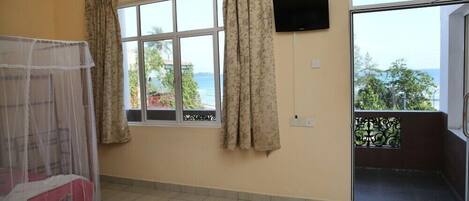 A room with a bed, a window with curtains, a TV mounted on the wall, and a balcony with a view.