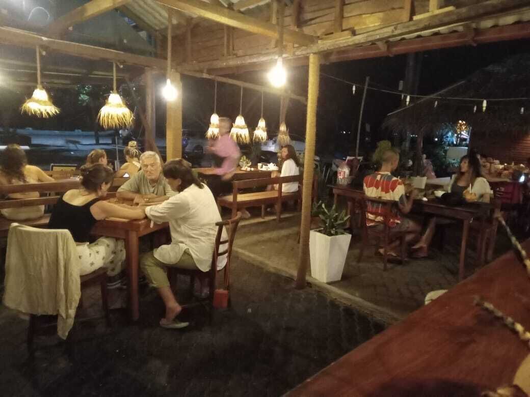 An outdoor dining area with wooden tables and chairs, hanging lights, and potted plants.