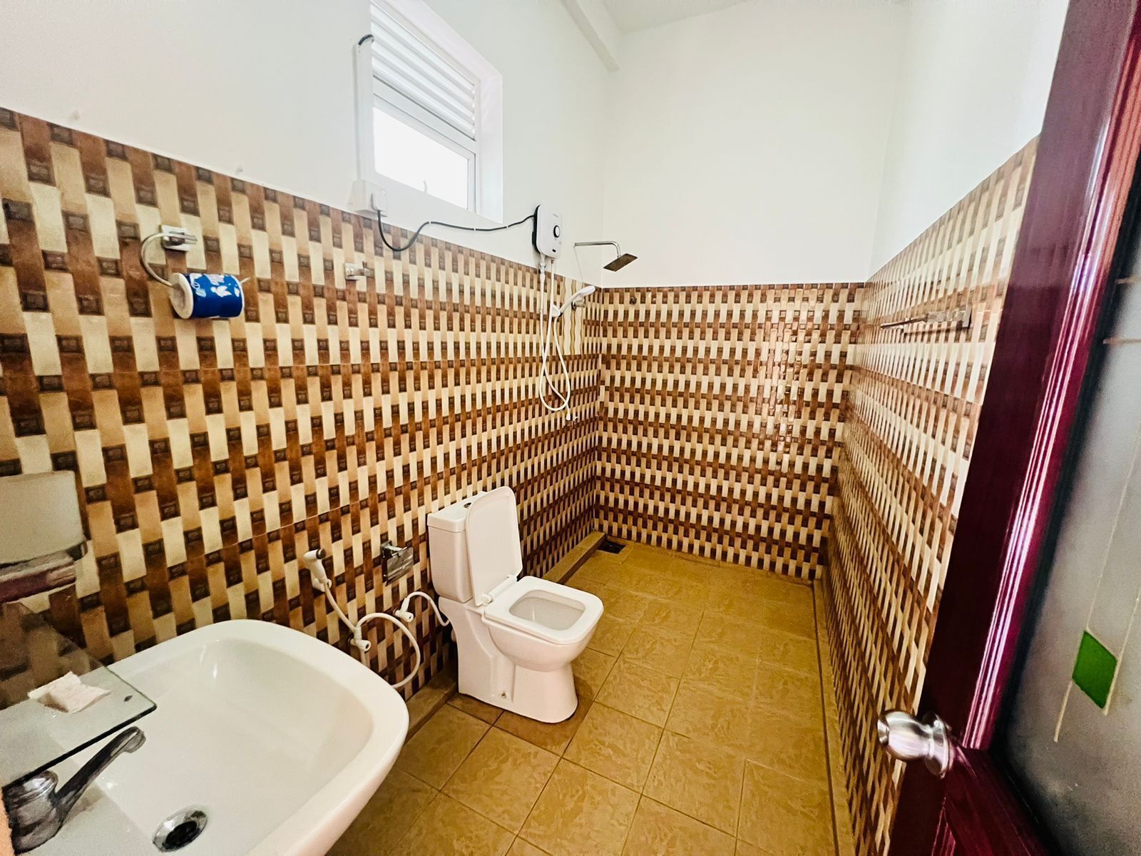 A small bathroom with a sink, toilet, and shower. The walls have a checkered tile pattern.